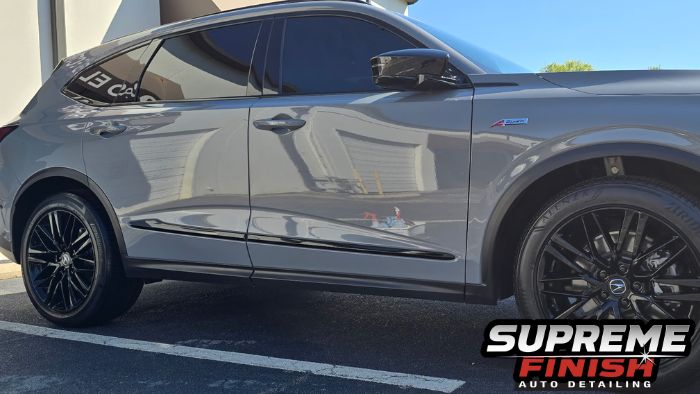 Side view of Acura MDX doors, dark windows, and black mirror with sunlight reflecting off the gray paint