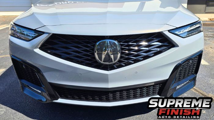 Front view of a metallic gray Acura MDX showing its sculpted hood, black grille, and Acura emblem