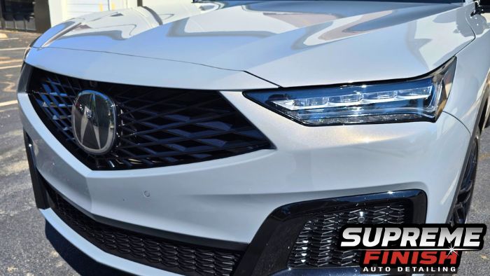 Angled close-up of the Acura MDX front bumper, black grille, and LED headlight in sunlight