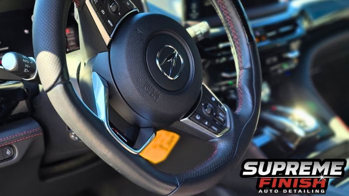 Acura MDX interior showing a perforated steering wheel, red stitching, and center console